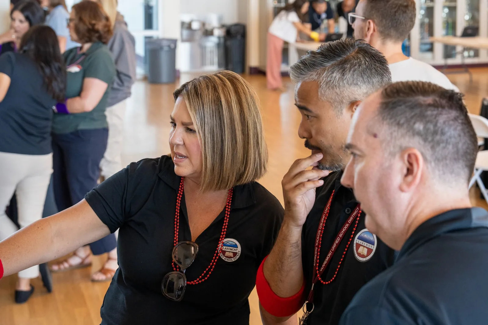 Three district staff in matching polos lean in together, listening intently during a session